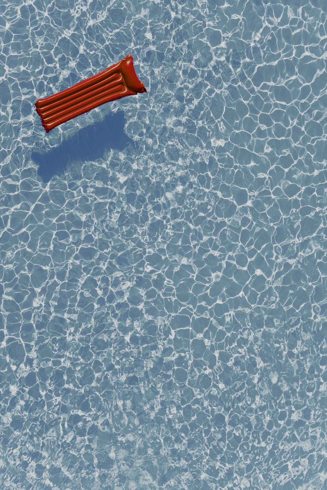A red pool float drifting alone on bright blue water.